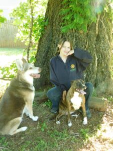 A Solgave caregiver spending time outdoors with two dogs beside a tree.