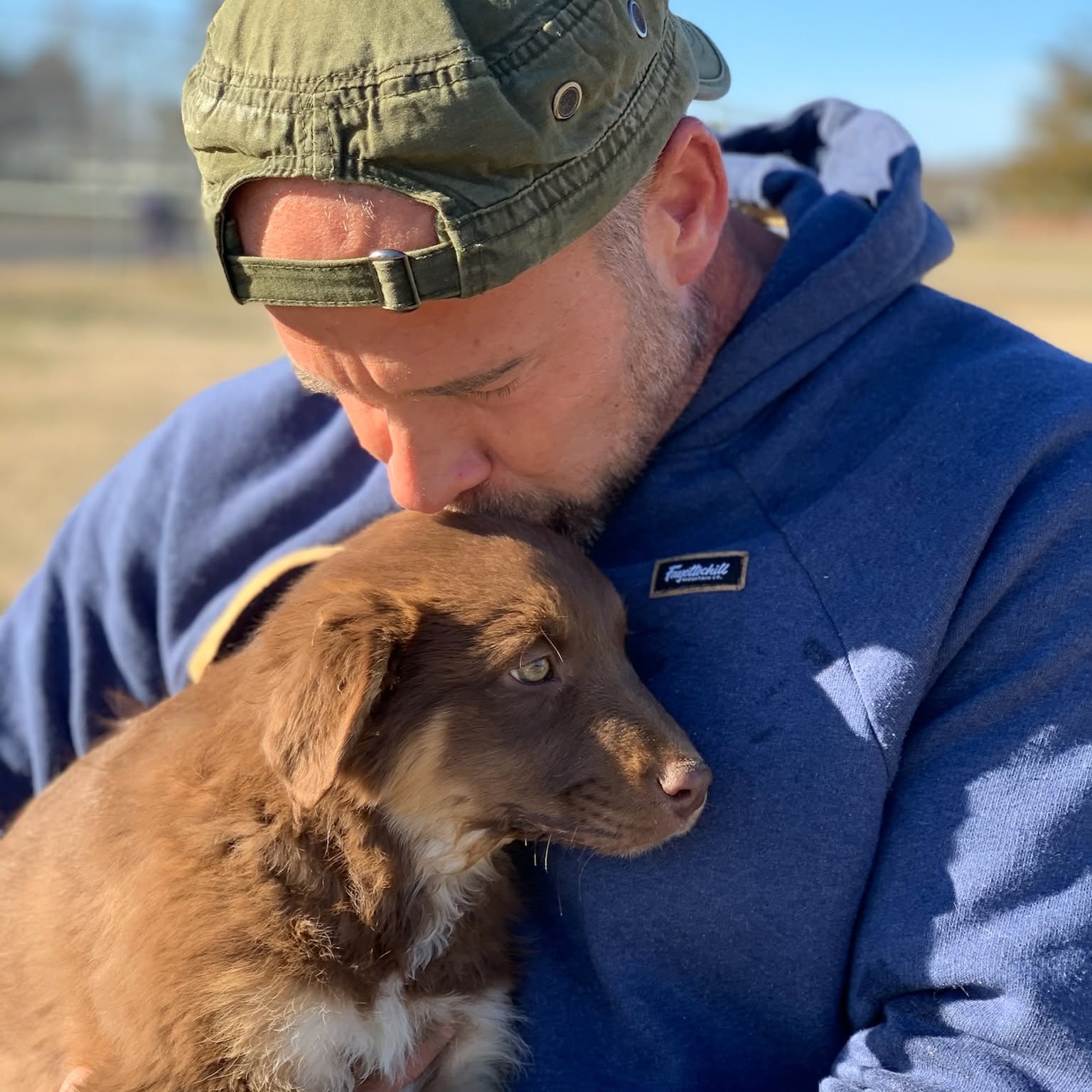 Jared holds a brown dog close while wearing a blue hoodie.