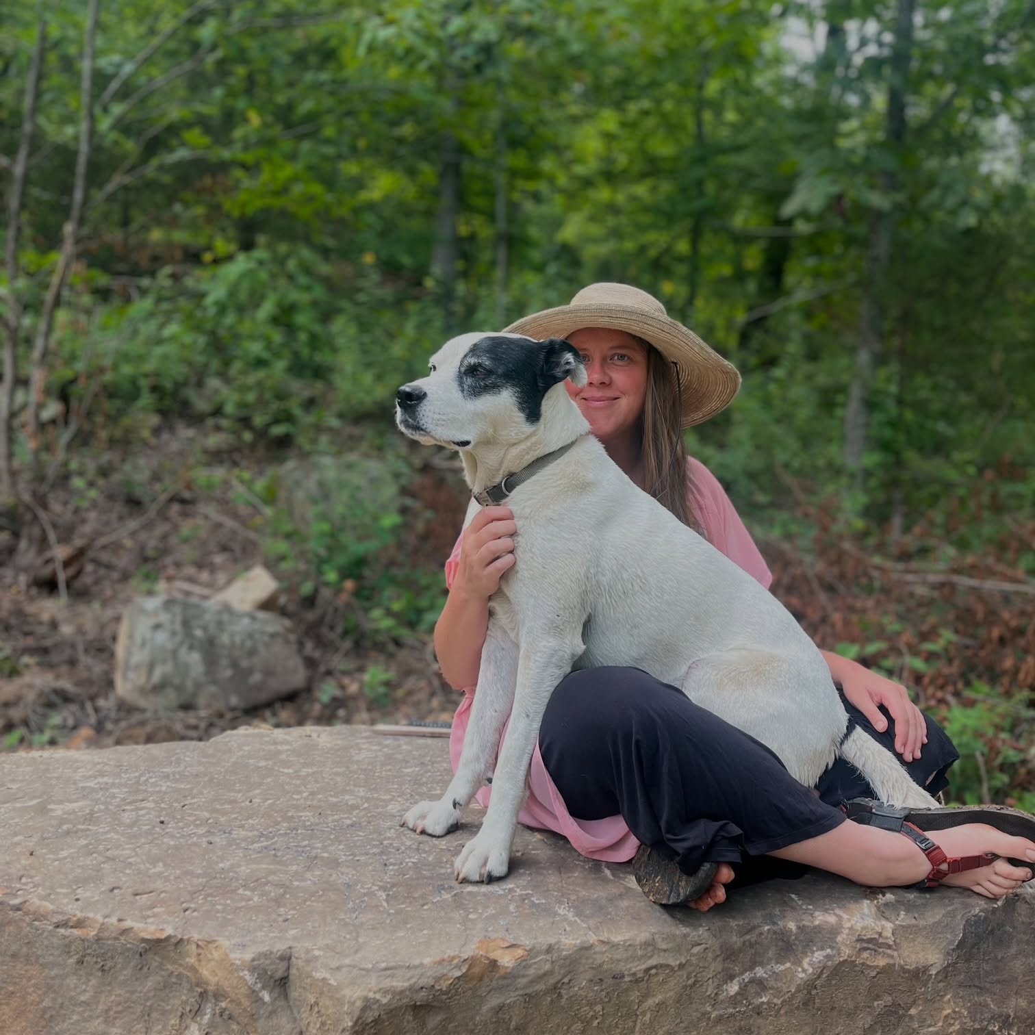 Sarah sits outdoors with a black-and-white dog leaning against her.