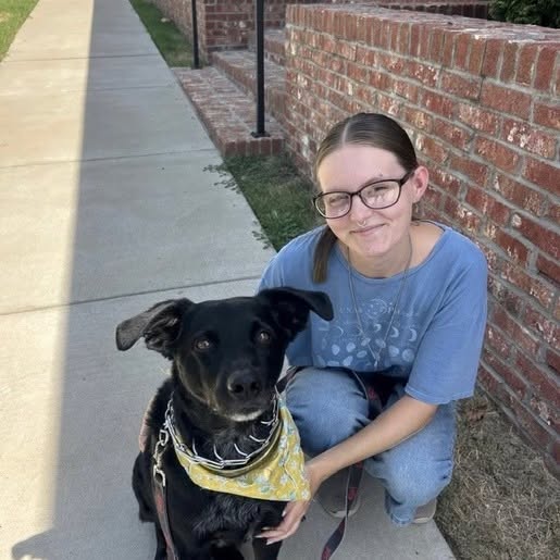 A Solgave team member kneels beside a black dog wearing a yellow bandana.